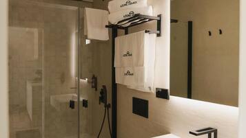 Un baño moderno con cabina de ducha de vidrio, un lavabo blanco con grifo negro y un espejo grande sobre el lavabo.