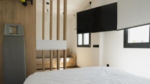 Une chambre d’hôtel moderne équipée d’un lit, d’un canapé, d’un téléviseur fixé au mur et d’une fenêtre laissant entrer la lumière naturelle.