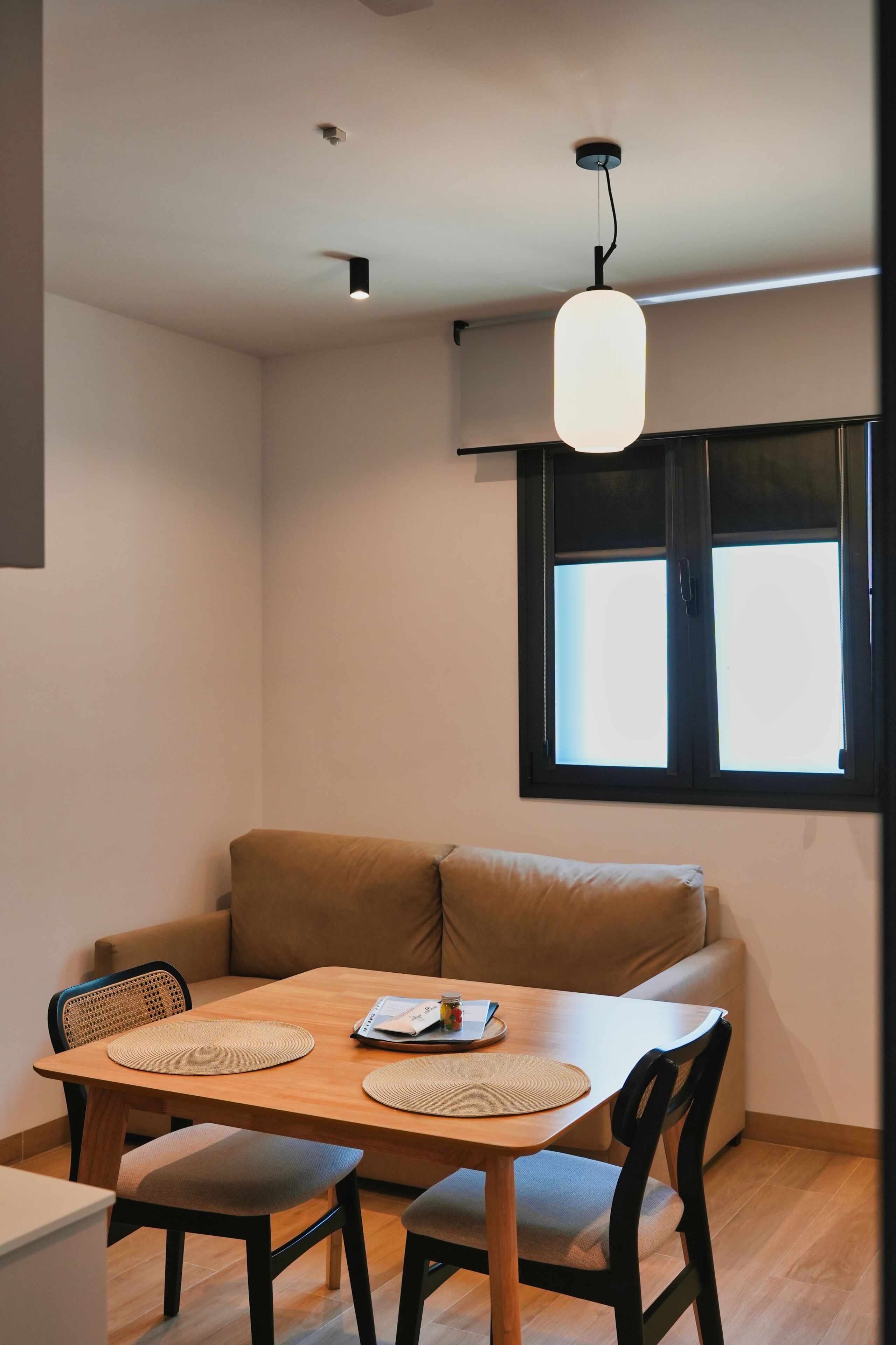 A dining area with a wooden table, four chairs, a brown sofa, and a window with blinds.