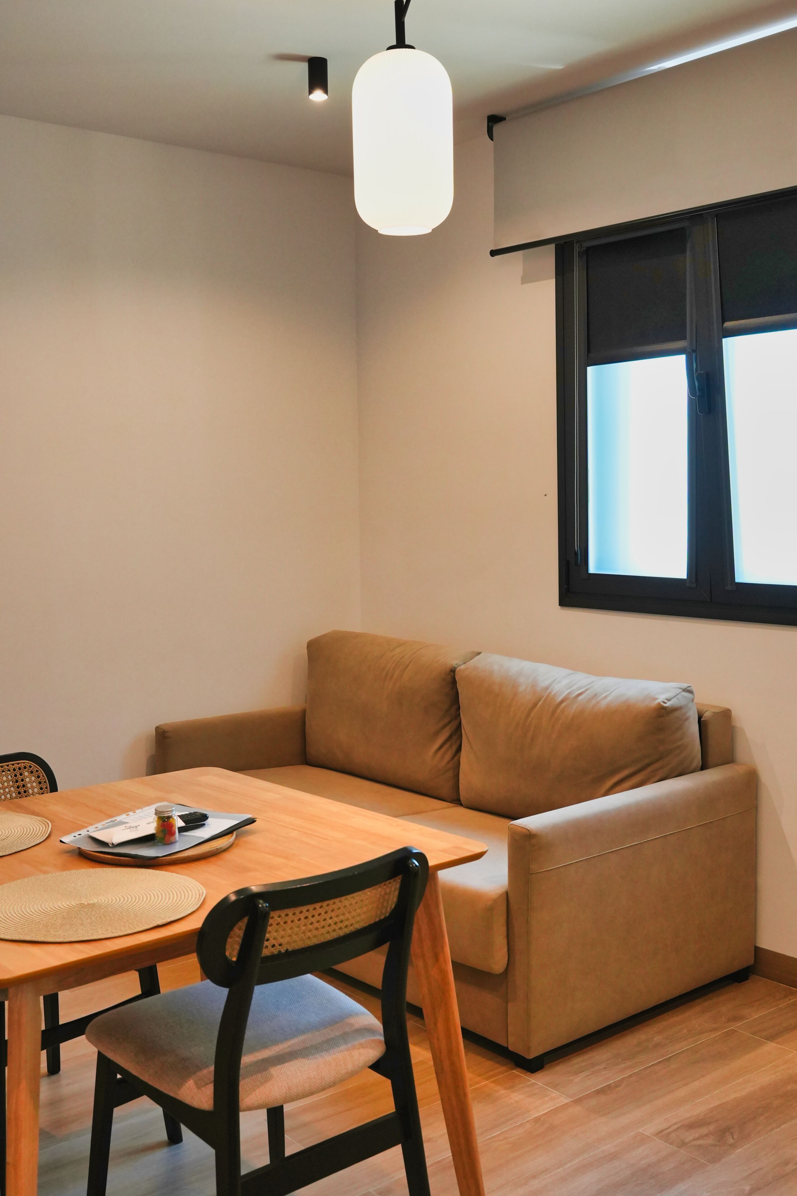 A room with a wooden dining table, a beige sofa, a single chair, and a window with blinds.