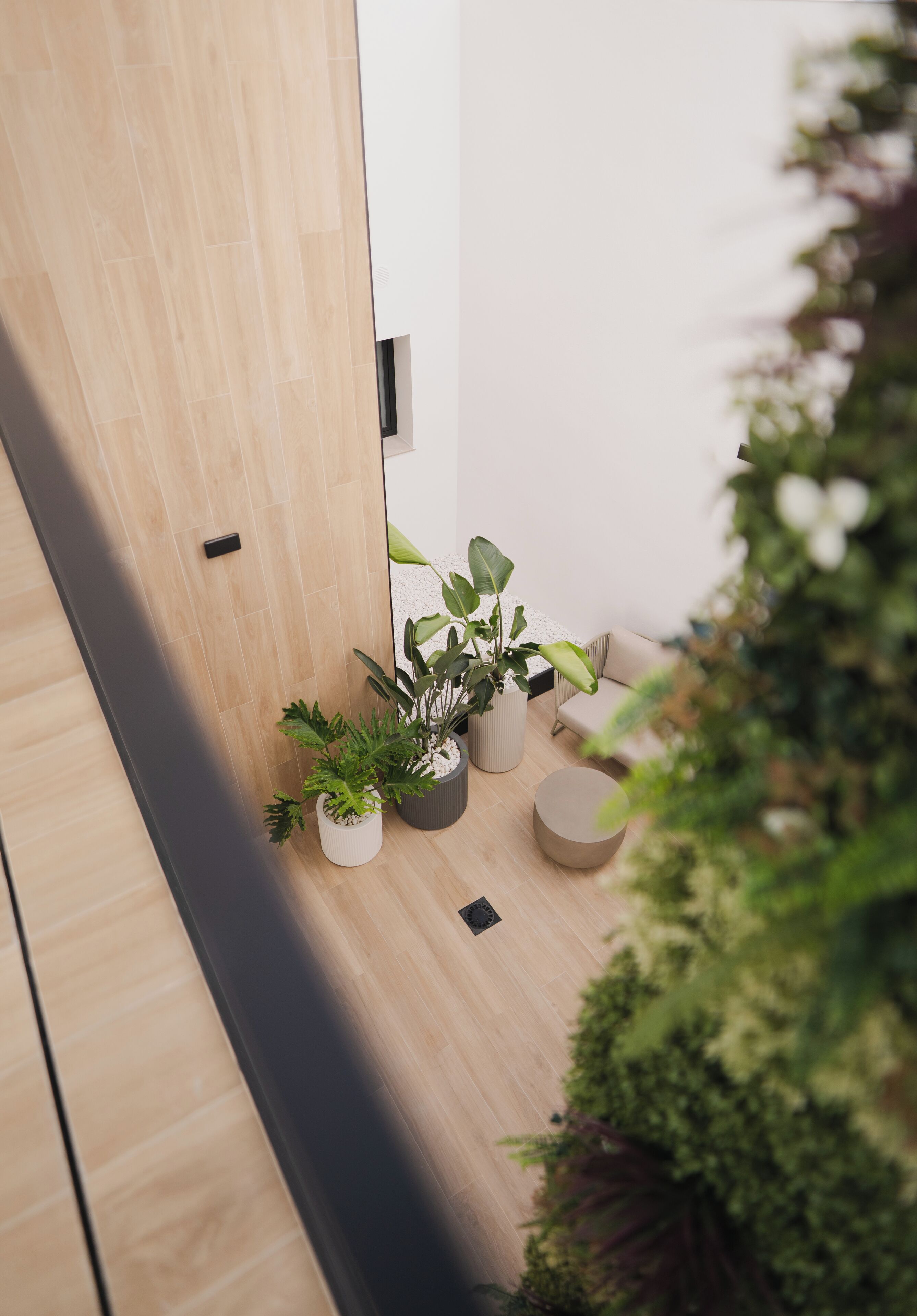 Een modern interieur met een houten vloer, een witte muur en een kleine zithoek met een bank en plantenpotten.