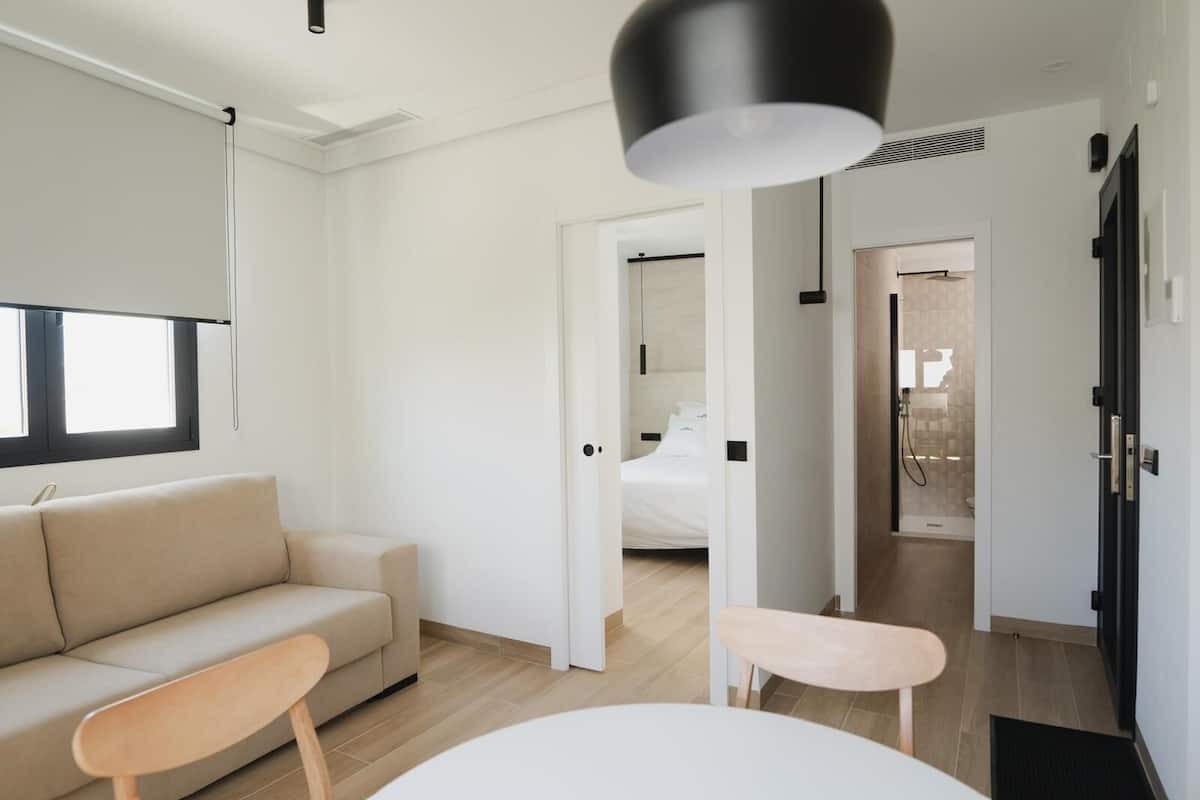 Una habitación de hotel moderna y minimalista con sofá, una pequeña mesa y una cama al fondo.