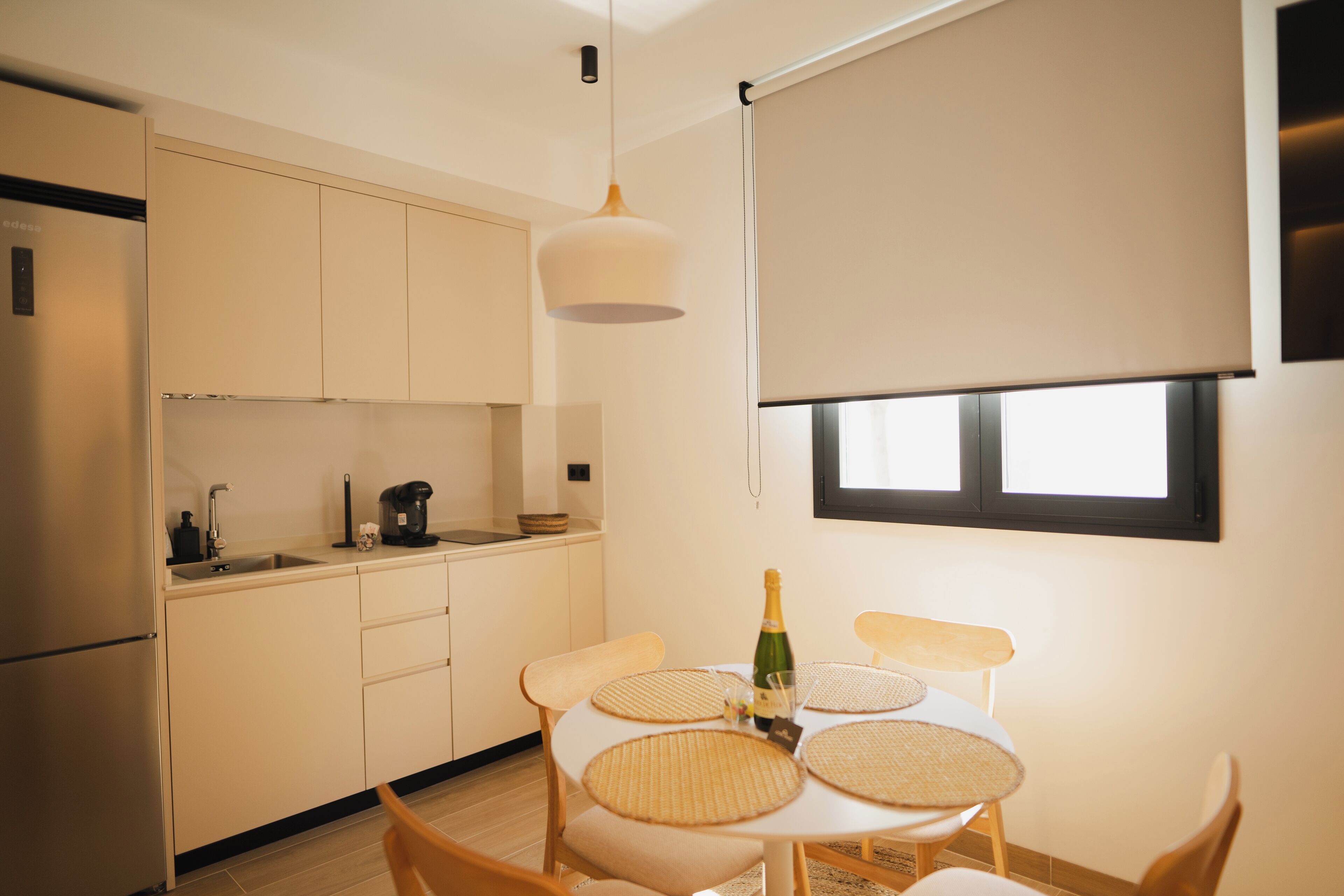 Une cuisine moderne avec un coin repas, comprenant une table avec quatre sets de table en fibres tressées, une bouteille de champagne et une machine à café.