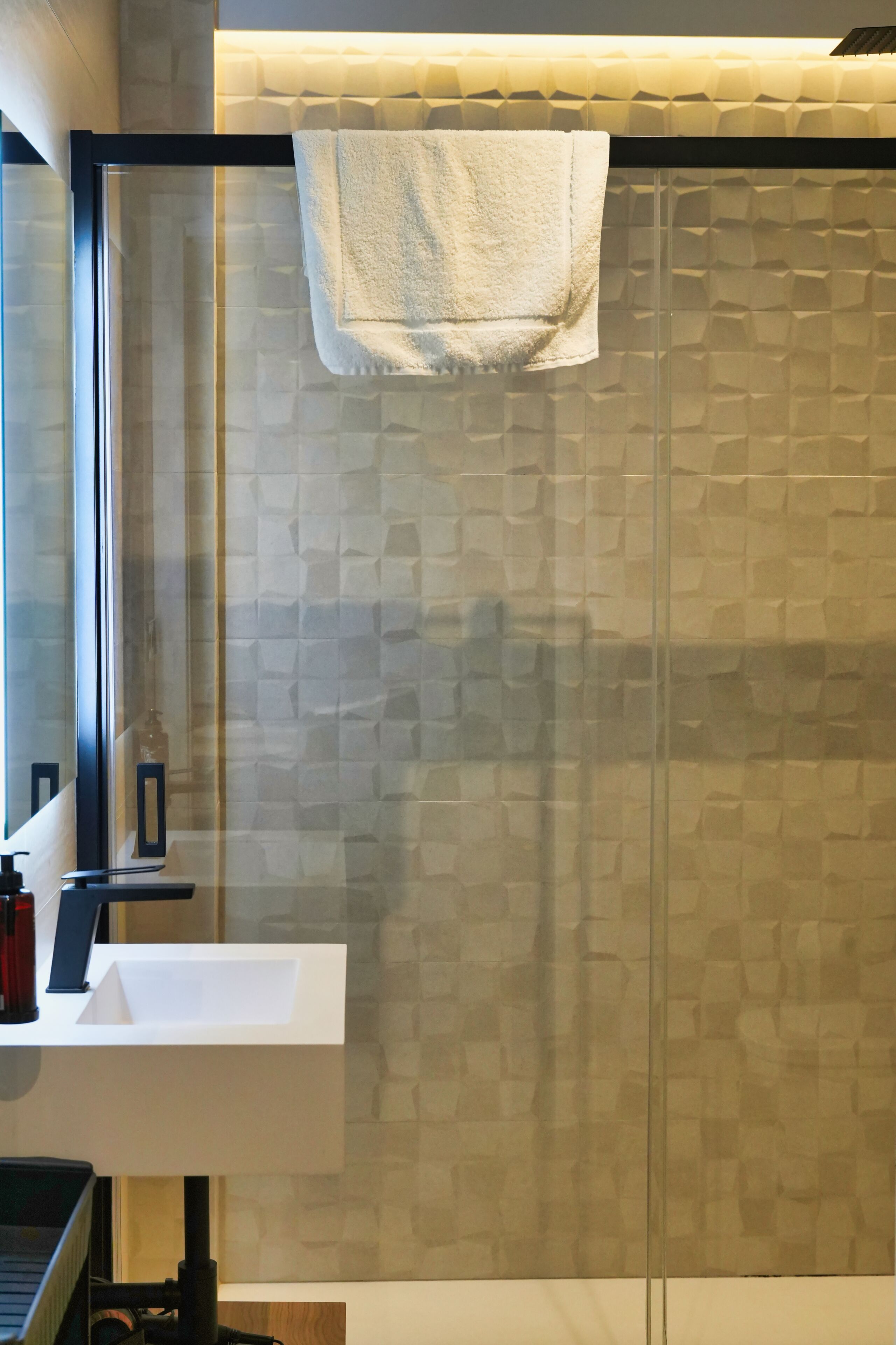A bathroom with a glass shower enclosure, a white sink, and a towel hanging on the shower door.
