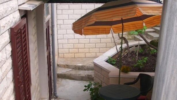 A small outdoor patio with a table and chairs, a striped umbrella, and a brick wall. - Apartment Korina (Pucisca)