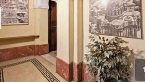 Un couloir doté d’un sol carrelé, de colonnes en marbre blanc et rouge, et de deux grandes peintures murales.