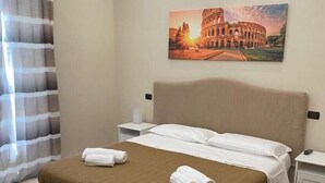 Ein Hotelzimmer mit Bett, einer Sitzbank, einem Gemälde des Kolosseums und einem Fenster mit Vorhängen.