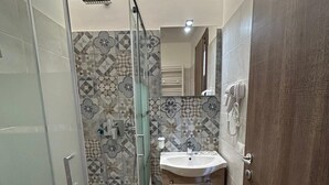 A modern bathroom with a glass shower enclosure, patterned tiles, and a wooden floor. - grimaldi  comfort   1 (ROMA)