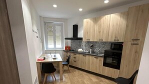 A modern kitchen with wooden cabinets, a dining table with chairs, and a built-in oven. - grimaldi  comfort   1 (ROMA)