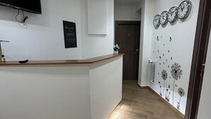 Un espace d’accueil doté d’un téléviseur à écran plat, d’une pancarte de bienvenue, d’un comptoir d’accueil en bois et d’un mur orné d’horloges et de motifs de pissenlits.
