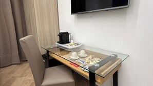 Une chambre moderne avec une table à plateau en verre, une chaise, un téléviseur à écran plat fixé au mur et une armoire.