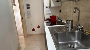 A kitchen with a stainless steel sink, wooden cabinets, a clock on the wall, and a tiled floor.