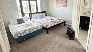 Une chambre avec deux lits, une fenêtre, un tableau et une salle de bain visible à travers une porte ouverte.