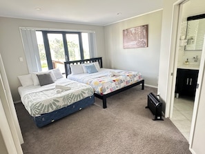 Une chambre avec deux lits, une fenêtre, un tableau et une salle de bain visible à travers une porte ouverte.