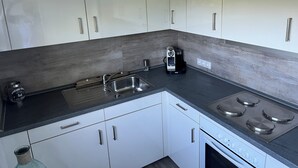 Una cocina moderna con armarios blancos, un lavamanos de acero inoxidable, una cafetera y una estufa.