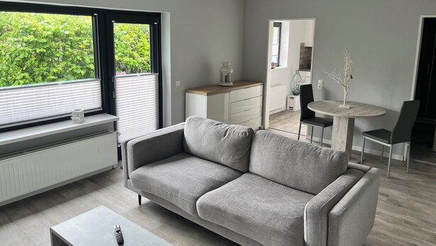 Una sala de estar moderna con un sofá gris, una mesita de centro y un comedor con una mesa redonda y sillas.