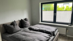 Un dormitorio con una cama doble, dos almohadas, una ventana con persianas y un radiador.