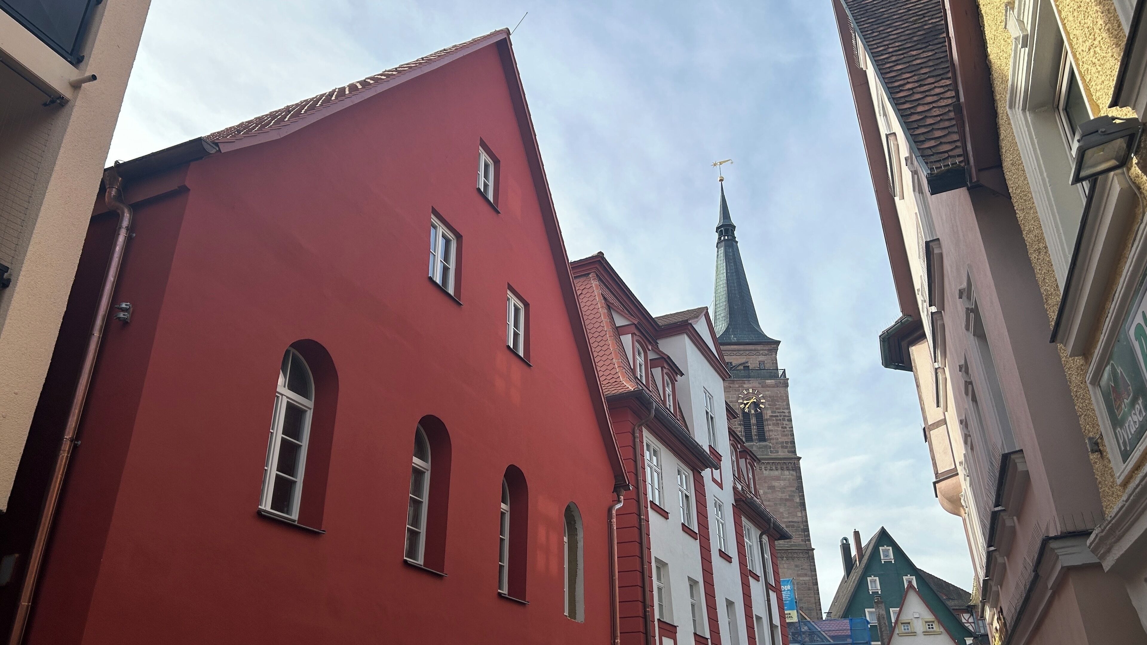 Uma rua estreita com edifícios vermelhos e brancos, um campanário de igreja e uma torre com relógio.