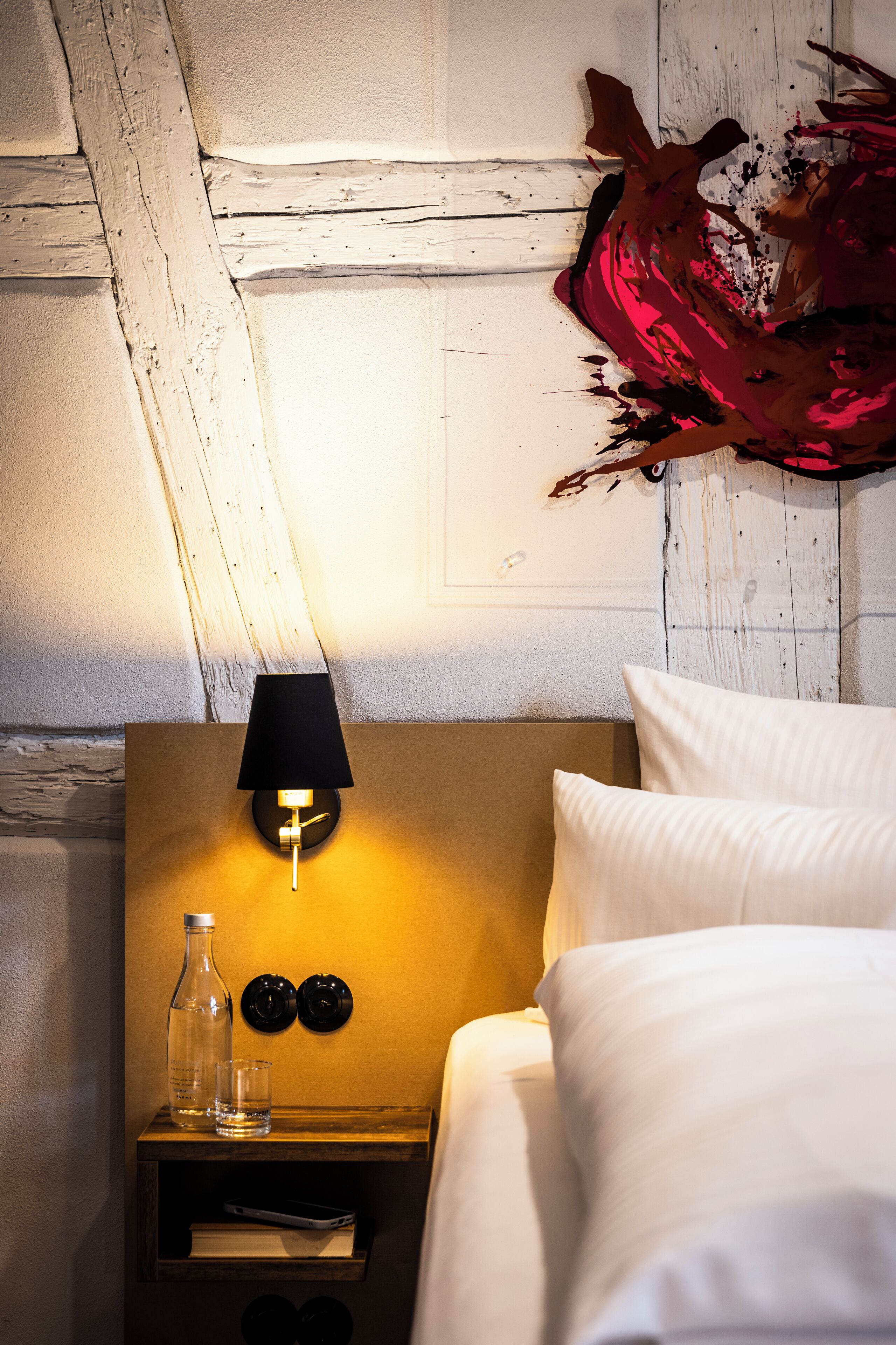 A neatly made bed with white linens, a bedside table with a lamp, a bottle, and two glasses.