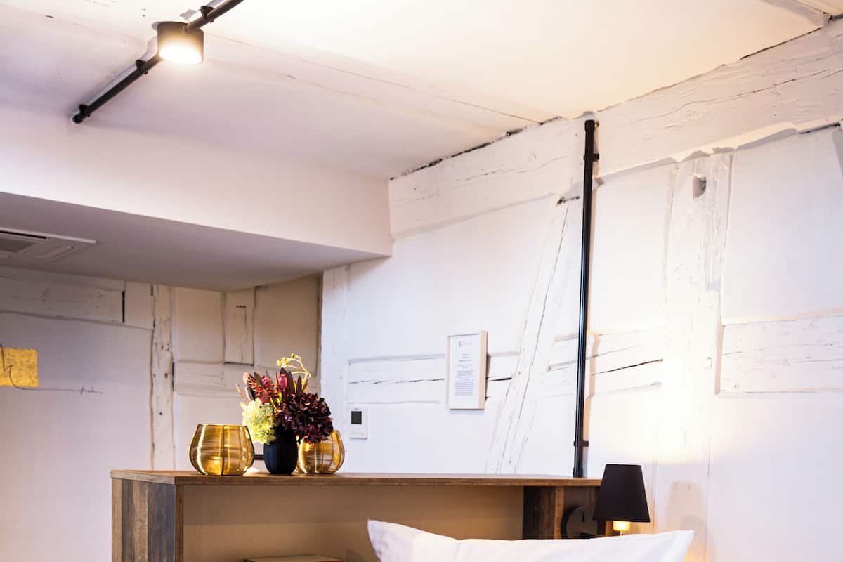 A bedroom with a wooden headboard, a bed with white linens, a bedside table with books, and a wall-mounted lamp.