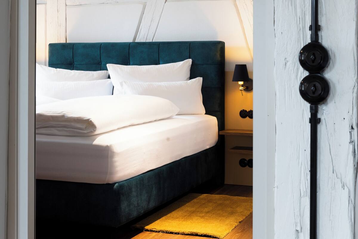 A bedroom with a teal upholstered headboard, white bedding, and a wooden floor.