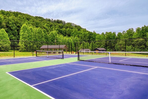 A tennis court with a net, surrounded by a fence and trees.
