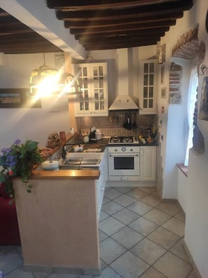 A compact kitchen with white cabinets, a central island, a stove, and a hanging light fixture.