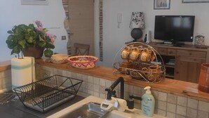 Et køkken med vask, en kurv med brød, en plante og et fjernsyn i baggrunden.