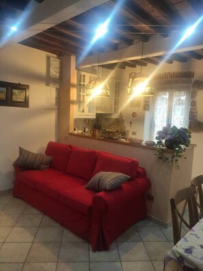 A red sofa in a living room with a kitchen in the background.