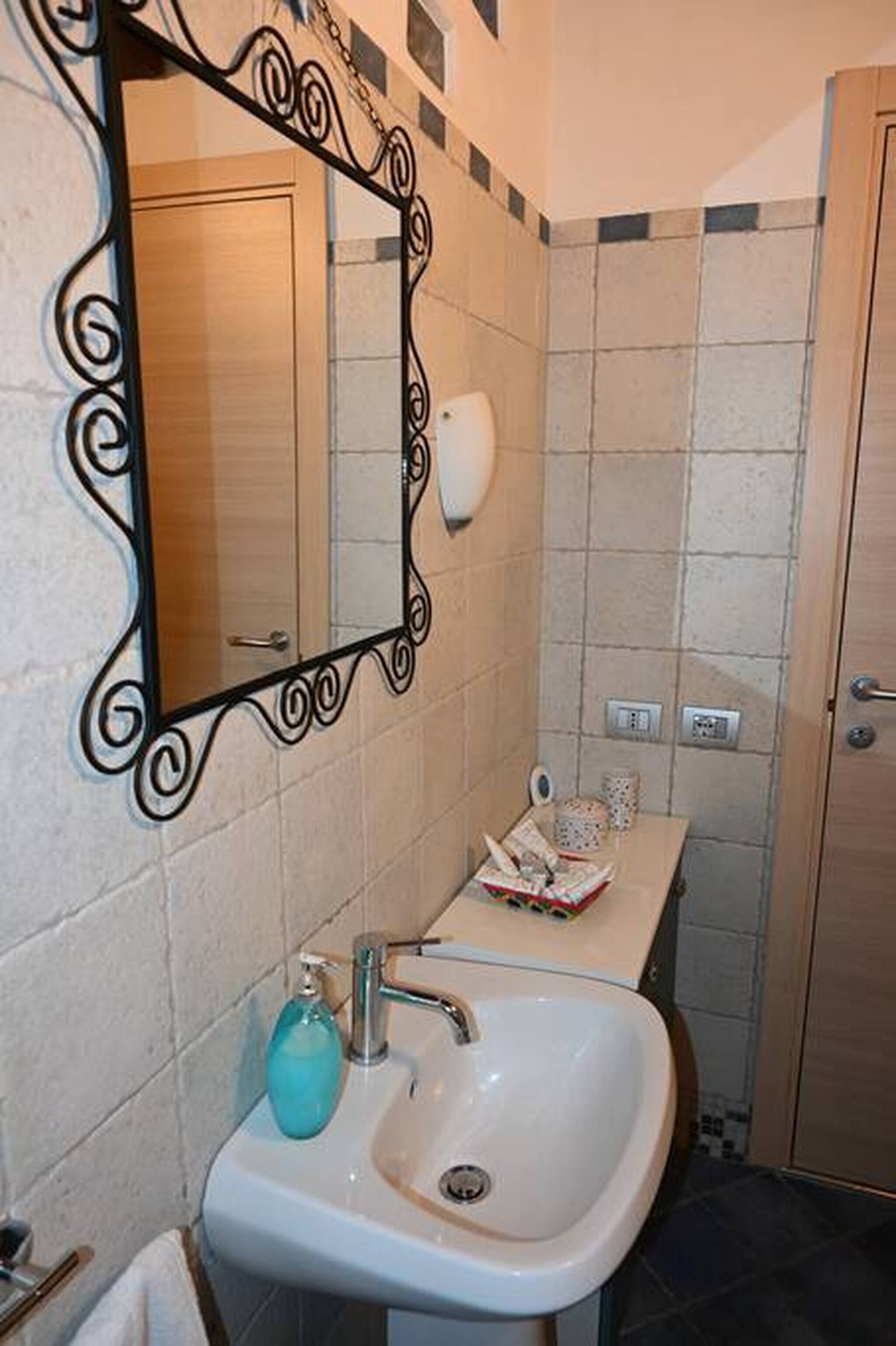 Un bagno con lavandino bianco, uno specchio con cornice decorativa, un portascopevoli e un water.