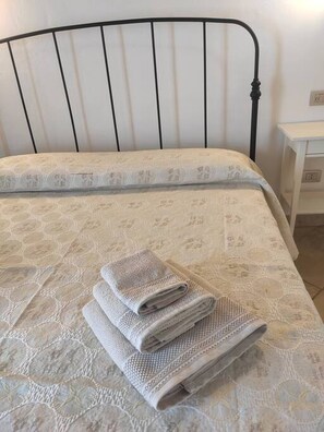 A bed with a patterned bedspread, a metal headboard, and a folded towel on the bed.
