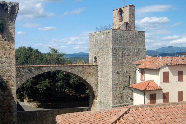 A stone bridge with an arch, a tower, and buildings with red-tiled roofs.