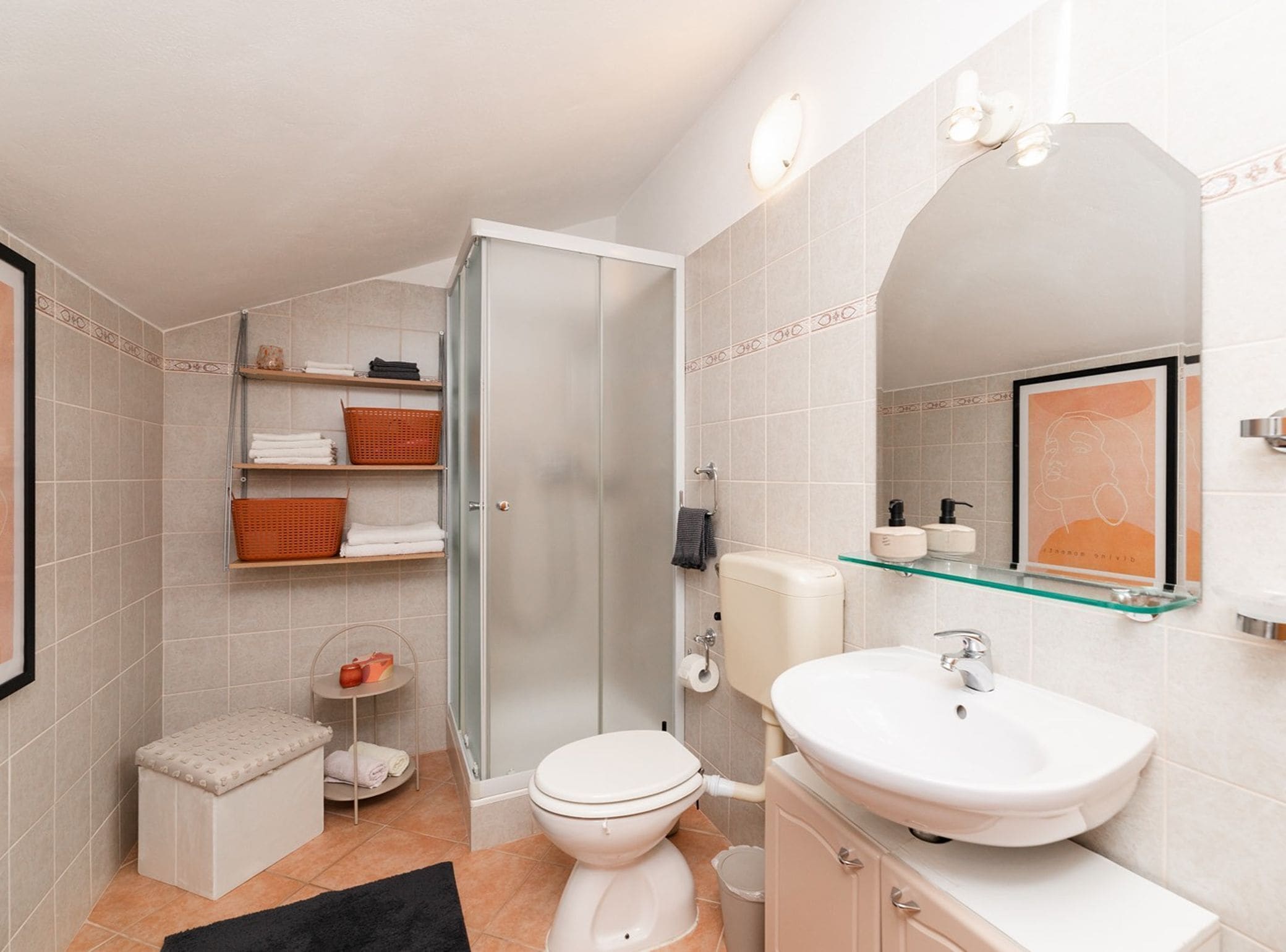 A modern bathroom with a glass shower enclosure, a white toilet, a sink with a glass shelf, and a framed artwork above the mirror.