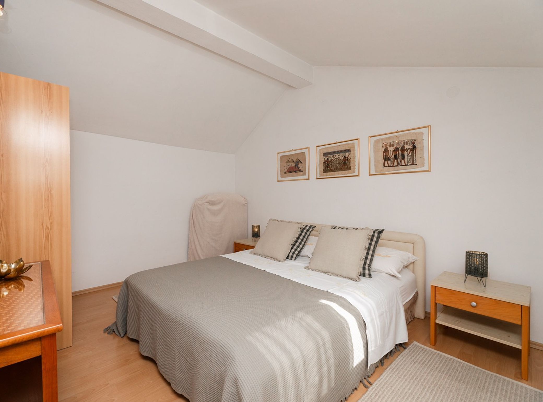 A bedroom with a bed, bedside tables, a chair, and wall art.