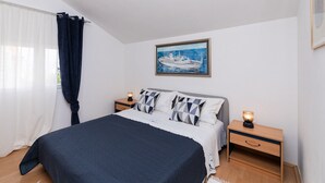 A bedroom with a bed, two bedside tables, a nightstand, a window with curtains, and a painting on the wall. - Apartments Roda - (Supetar)