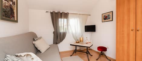 Une pièce confortable avec un canapé, une petite table sur laquelle se trouvent une bouteille et un verre, un téléviseur et une armoire.