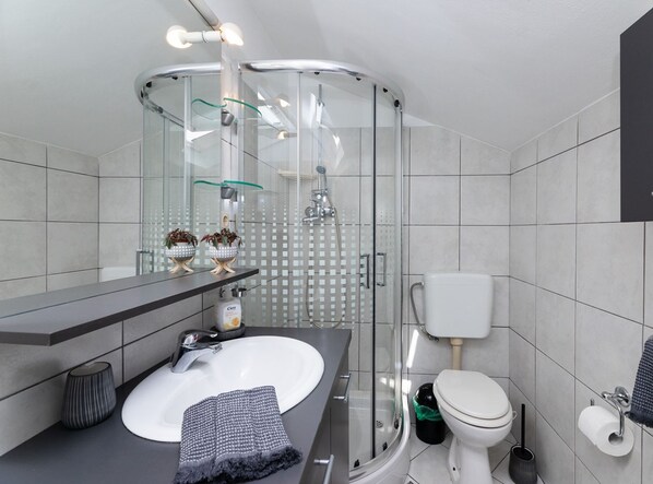 A modern bathroom with a glass-enclosed shower, a white sink, and a toilet.