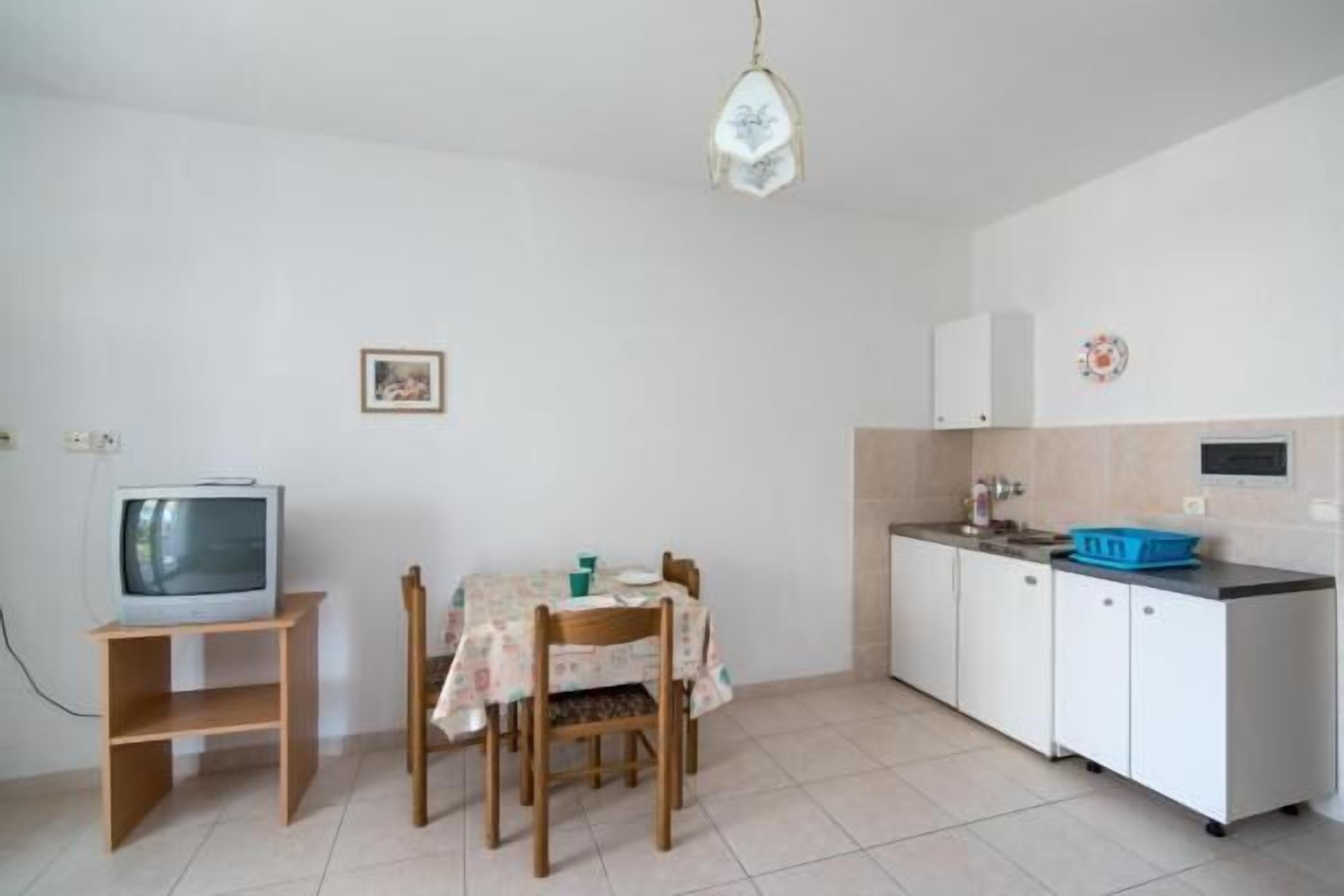 Eine kleine Küche mit Esstisch, Stühlen, einem Fernseher auf einem Schrank und Schränken.