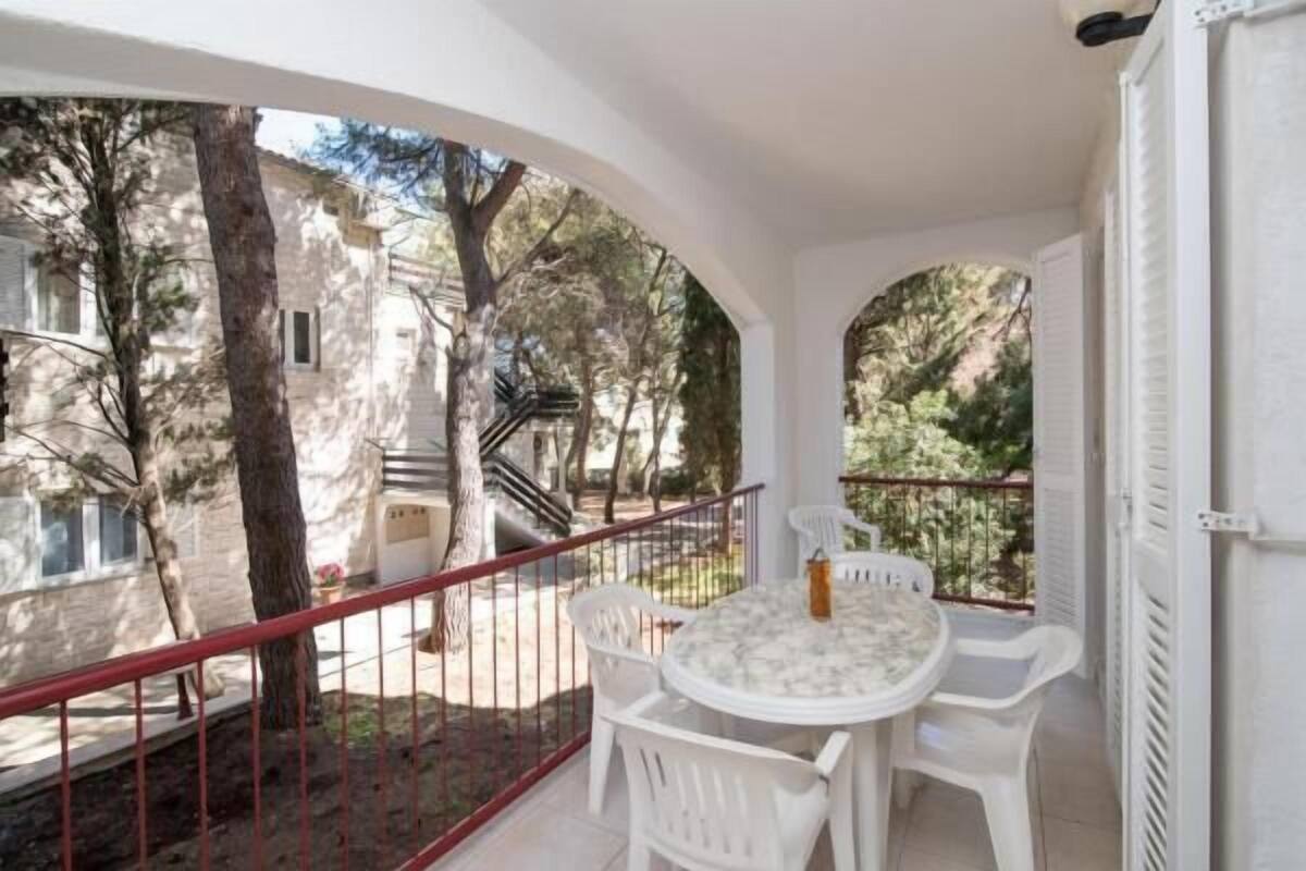 A balcony with a table and chairs, overlooking a courtyard with trees and a building.