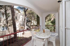 Ein Balkon mit Tisch und Stühlen, der auf einen Innenhof mit Bäumen und einem Gebäude blickt.