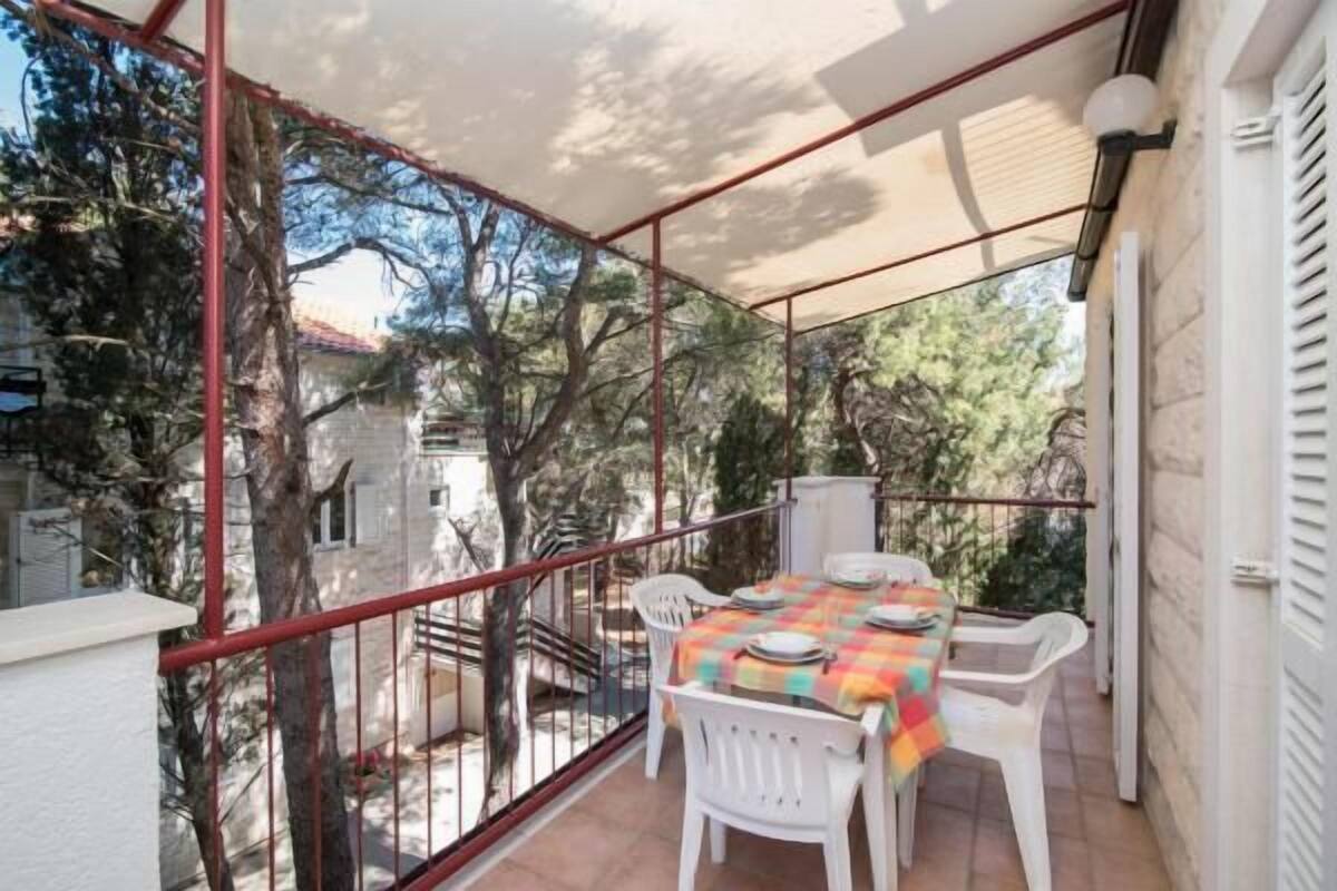 A balcony with a table set for dining, white chairs, and a view of trees and buildings.