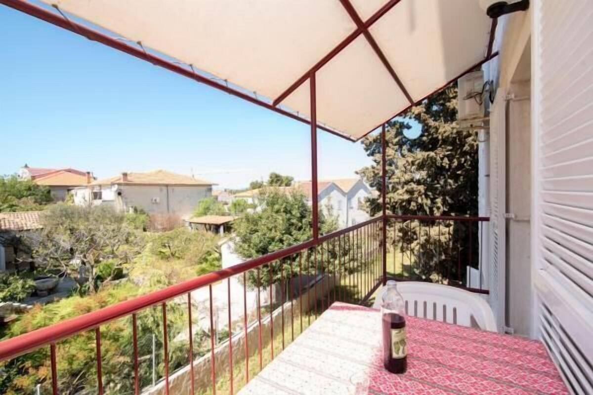 A balcony with a red railing, a table with a patterned tablecloth, and a bottle.