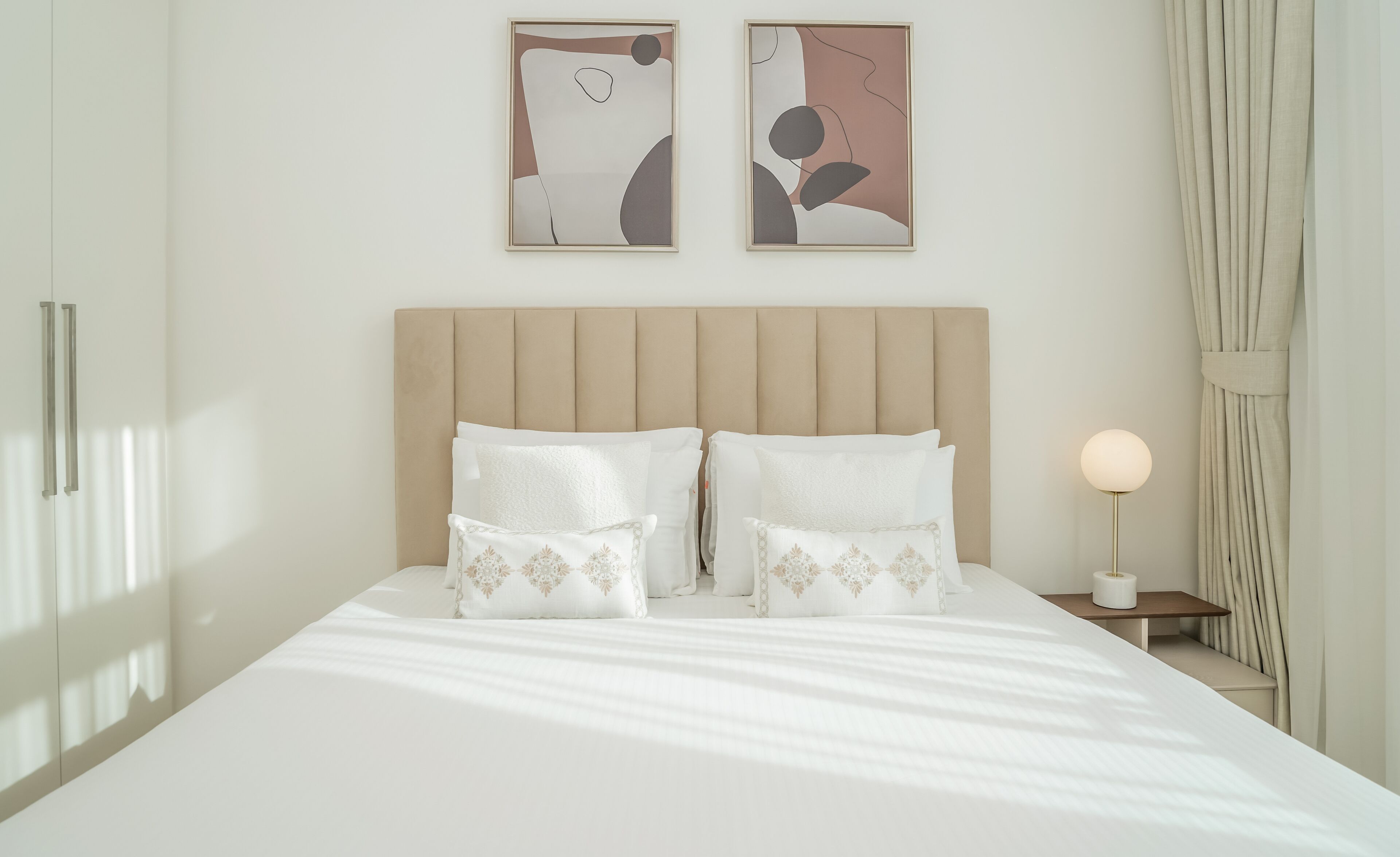 A neatly made bed with two pillows, a bedside table with a lamp, and abstract artwork on the wall.