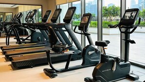 Een sportschool met meerdere loopbanden en elliptische trainers, grote ramen met uitzicht op de stad, en een modern interieur.