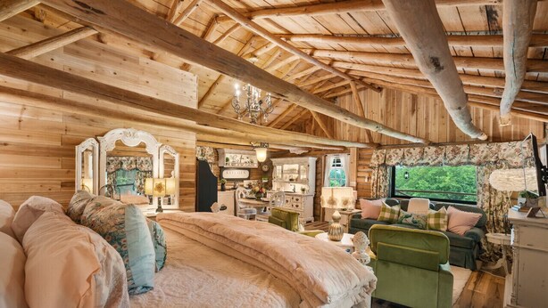 Interior acogedor de una cabaña de madera con una cama grande, un sillón verde y un televisor.