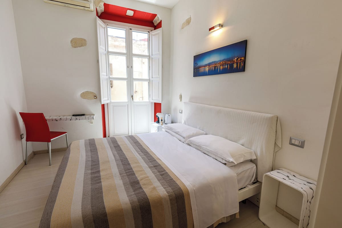 Ein Schlafzimmer mit Bett, Stuhl, Nachttisch, Fenster und einem Bild an der Wand.
