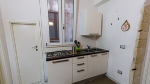 Une cuisine de taille réduite avec des meubles blancs, une cuisinière à gaz, un évier et une fenêtre.