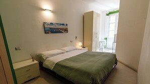 Une chambre à coucher avec un lit, des tables de chevet, une commode, un tableau et une vue sur l’extérieur.