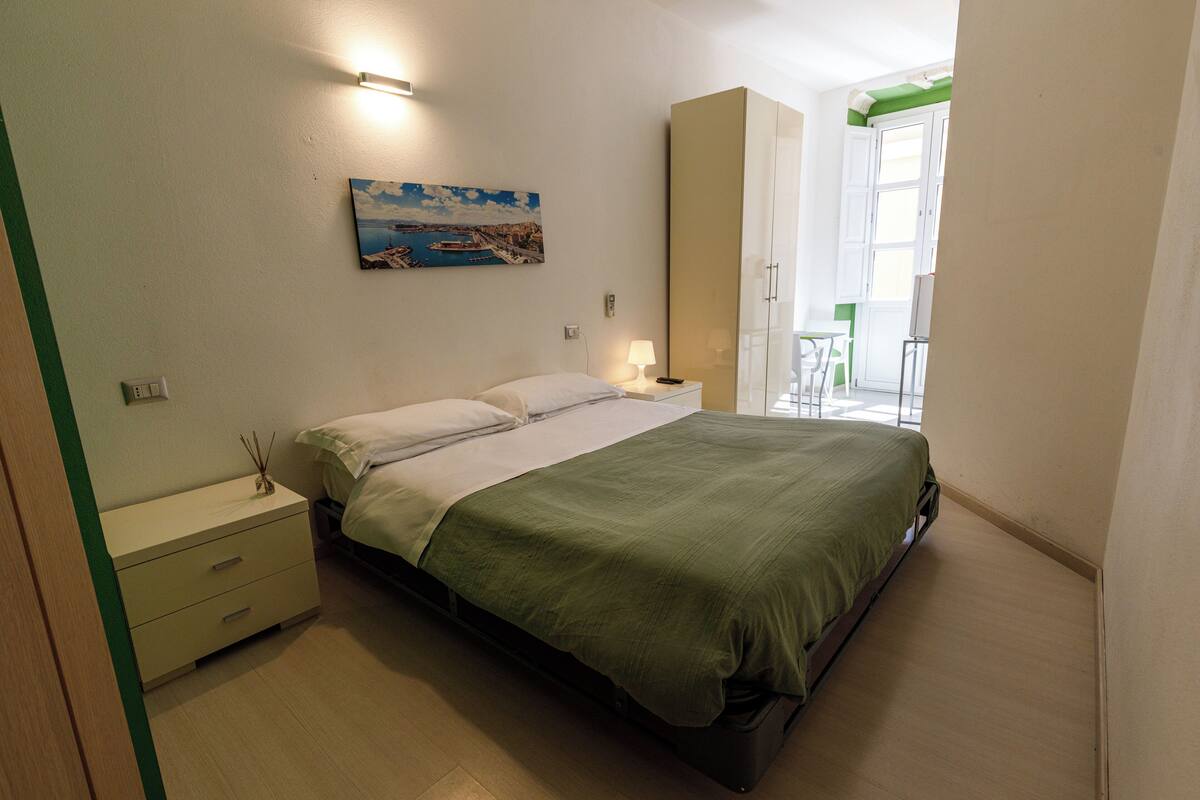 Ein Schlafzimmer mit Bett, Nachttischen, einem Gemälde und Blick ins Freie.