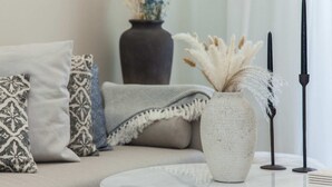 Un salón con sofá, cojines estampados, un jarrón con flores secas y candelabros.